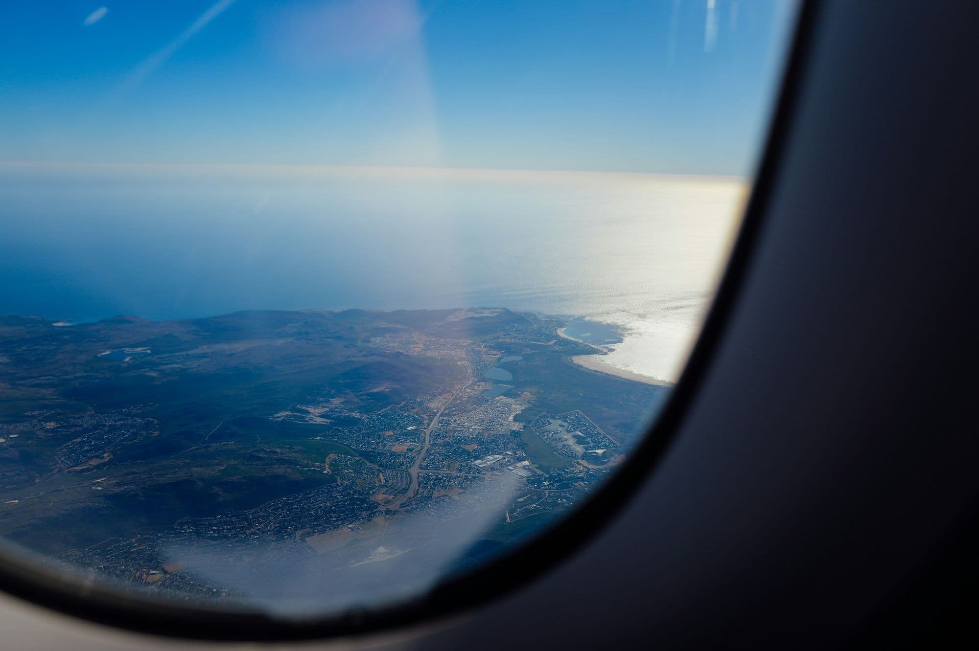 Vista da janela do avião sobre o litoral, com o mar e a costa lá embaixo.
